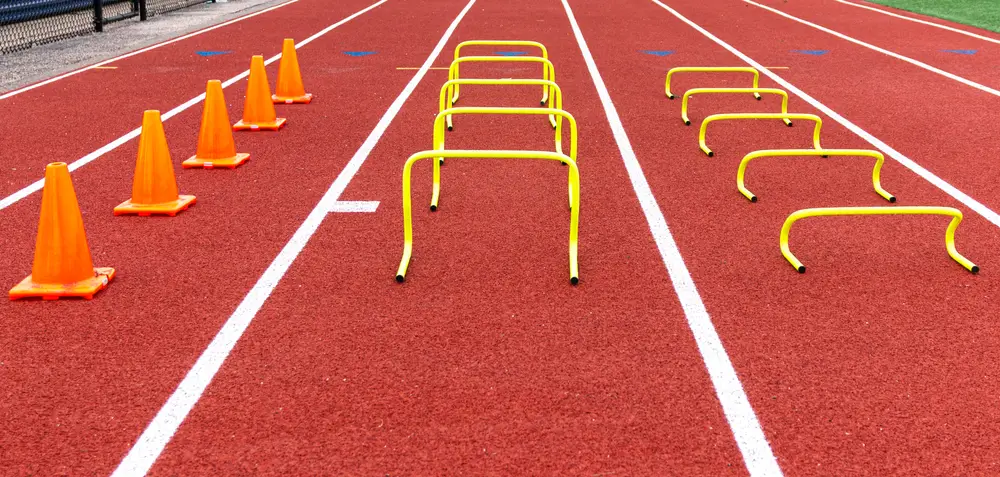 Orange sports cones and yellow hurdles marking running lanes on a red athletic track for fitness testing.