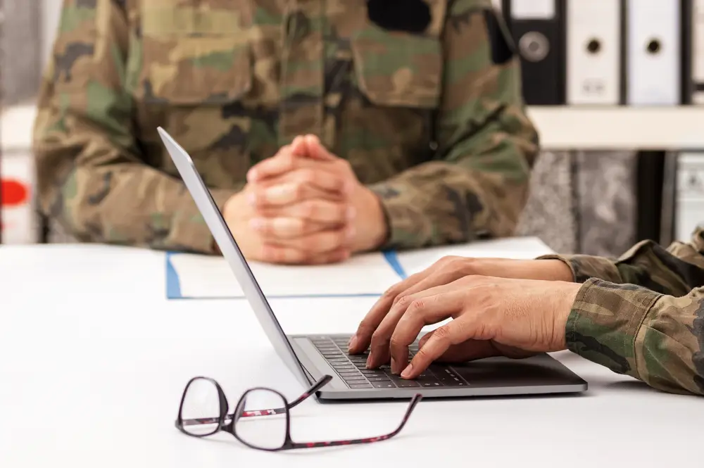 Military personnel conducting a recruitment office interview and online aptitude assessment on a laptop.