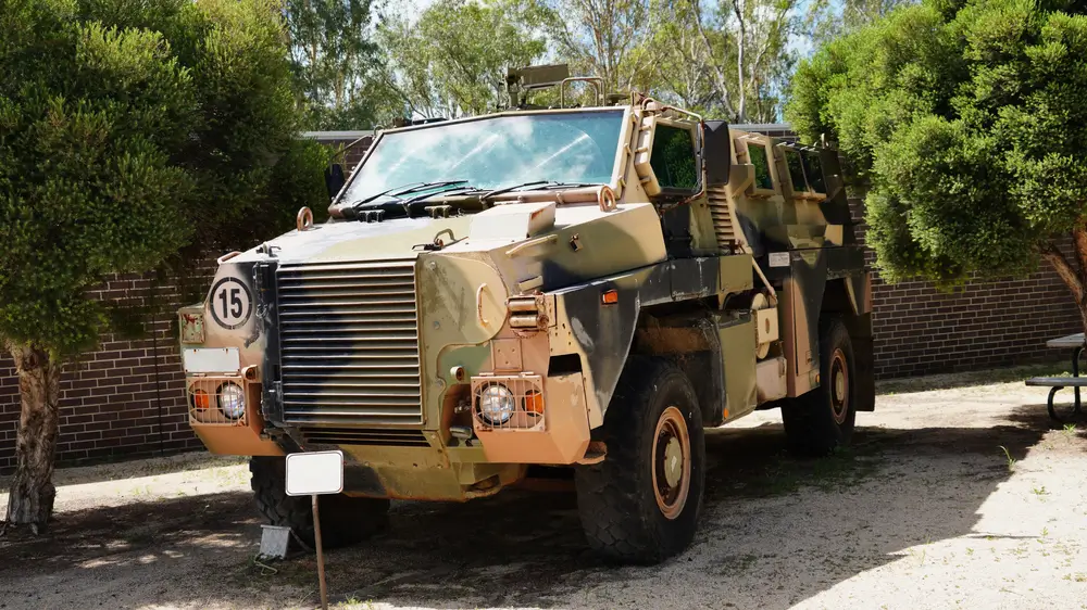 Camouflaged Bushmaster military vehicle parked at a military camp, showcasing army protected mobility.