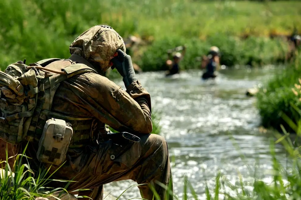 Soldier in camouflage gear watches others cross a river during a soldiers training military exercise.
