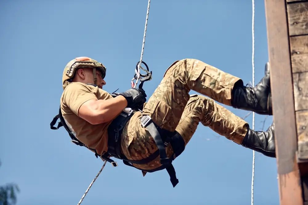 Soldier in uniform rappelling down a wooden wall during a military physical fitness and training exercise.