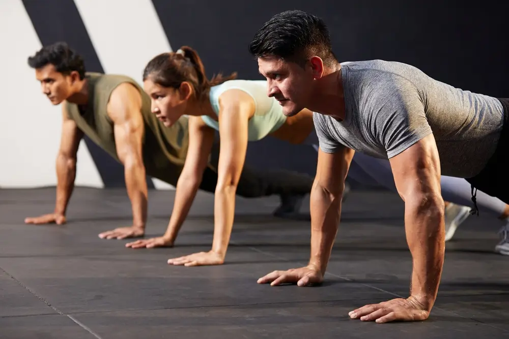 Focused athletes performing push-ups on a gym floor during a fitness competition.