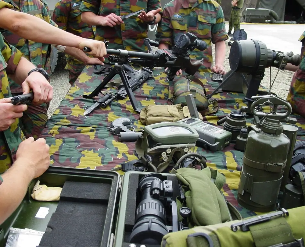 Army recruits examine military training gear and equipment on a table during an intake session at a training facility.