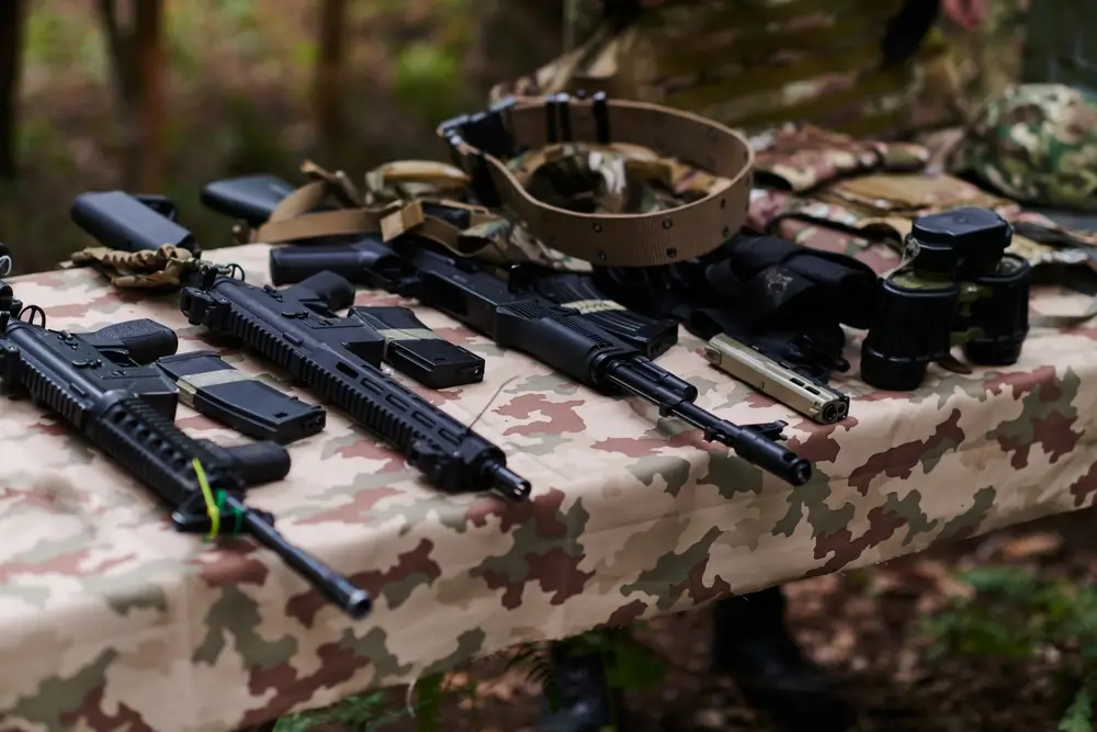 Military gear including an assault rifle and army rifle laid out on a camouflage table for a basic training inspection.