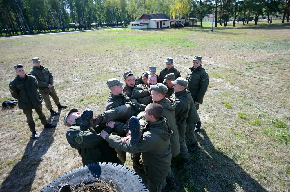 Army recruits on an obstacle course lifting a teammate during military recruit training.