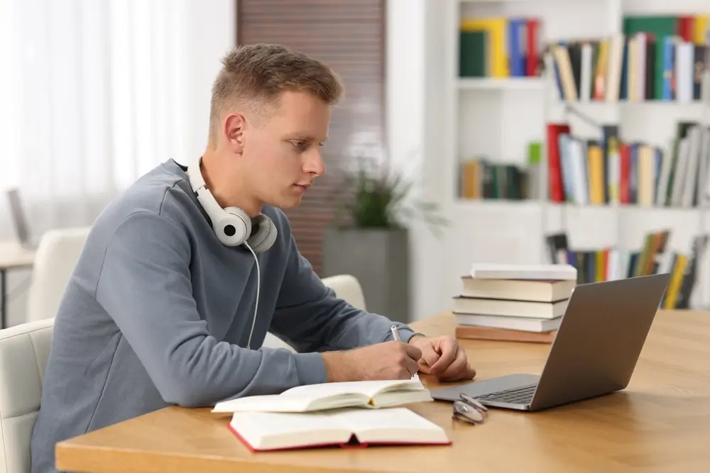 Student studying exam preparation at a desk with a laptop and textbooks, focused on preparing for an assessment test.