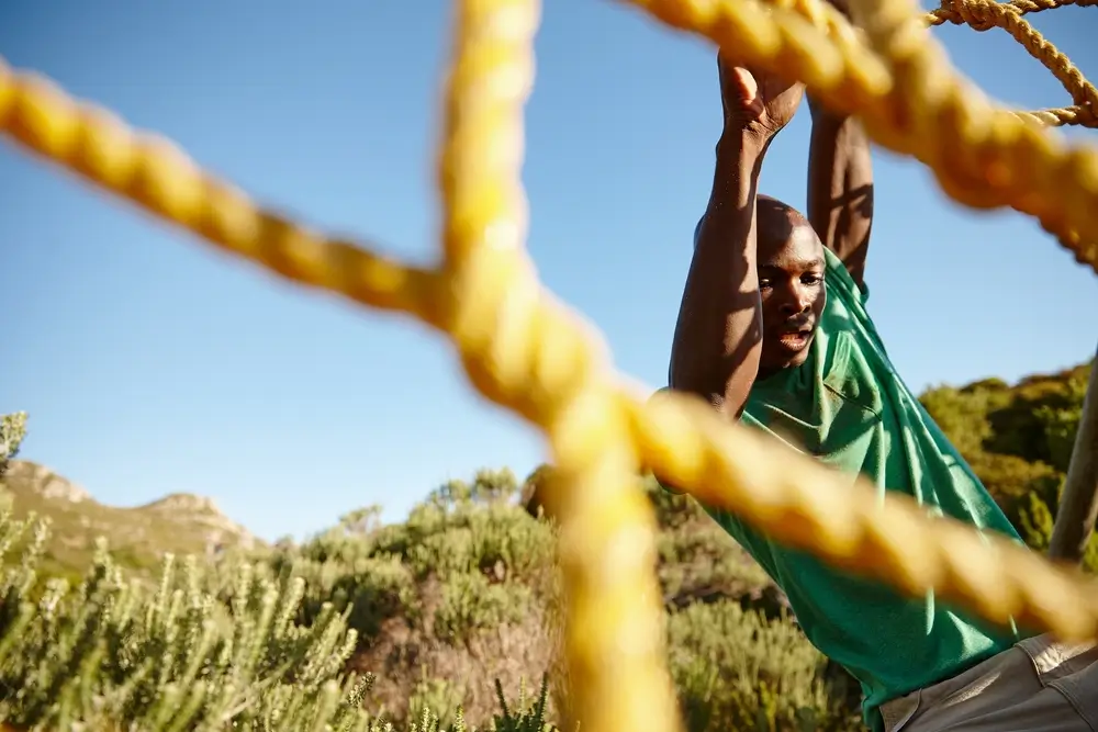 Military recruit climbs a yellow rope net during an outdoor physical fitness test for army training.
