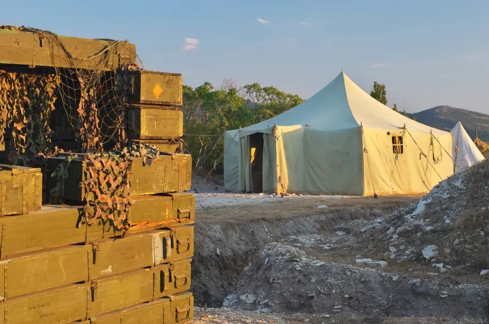 Stacked equipment crates and tan tents at a rugged military camp army base field training site.