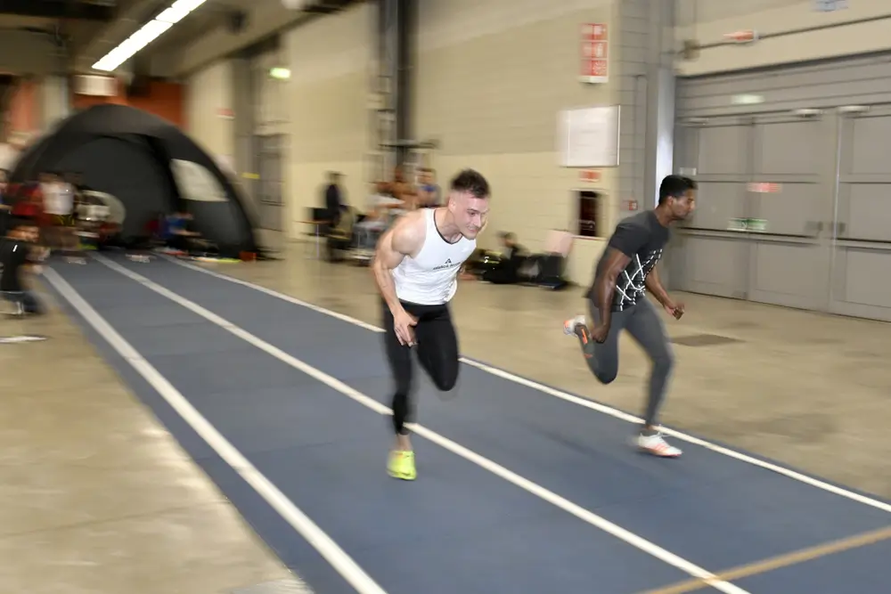 Athletes sprinting on an indoor track during a beep test shuttle run, demonstrating high intensity and speed.
