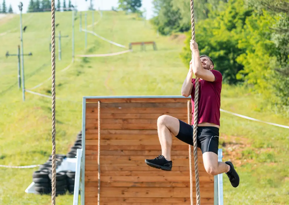 Soldier climbing a rope during a military fitness course, training to meet the required physical army standards.