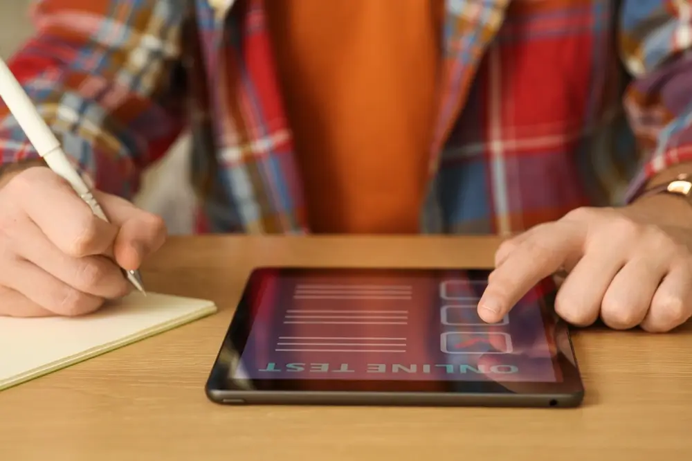 Candidate taking an online aptitude test computer assessment on a tablet while taking notes on paper.