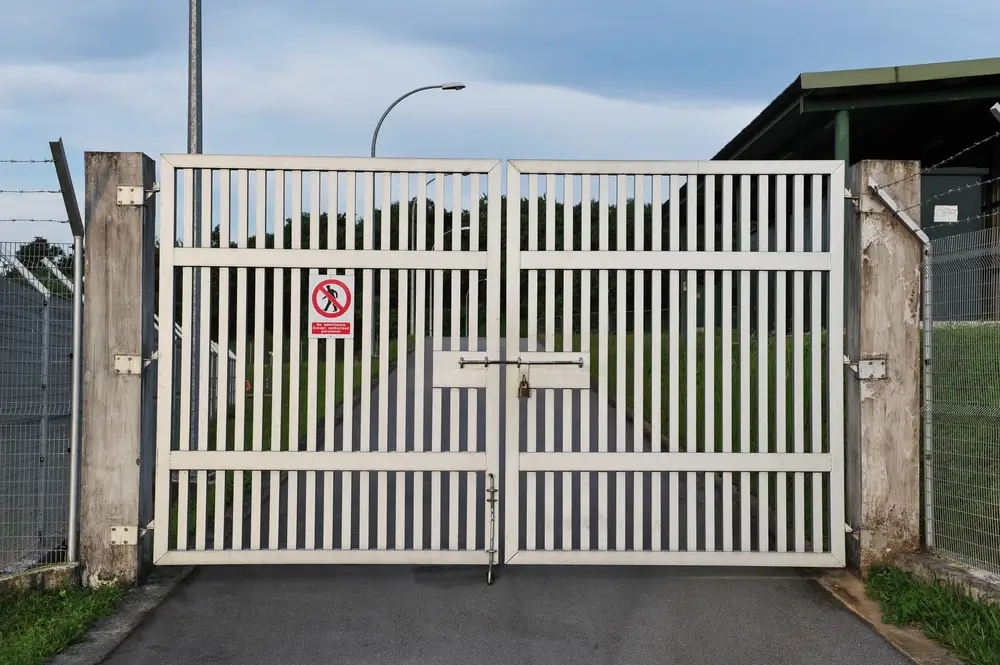 Closed white metal gate at a military base entrance with barbed wire fencing and a restricted entry sign.