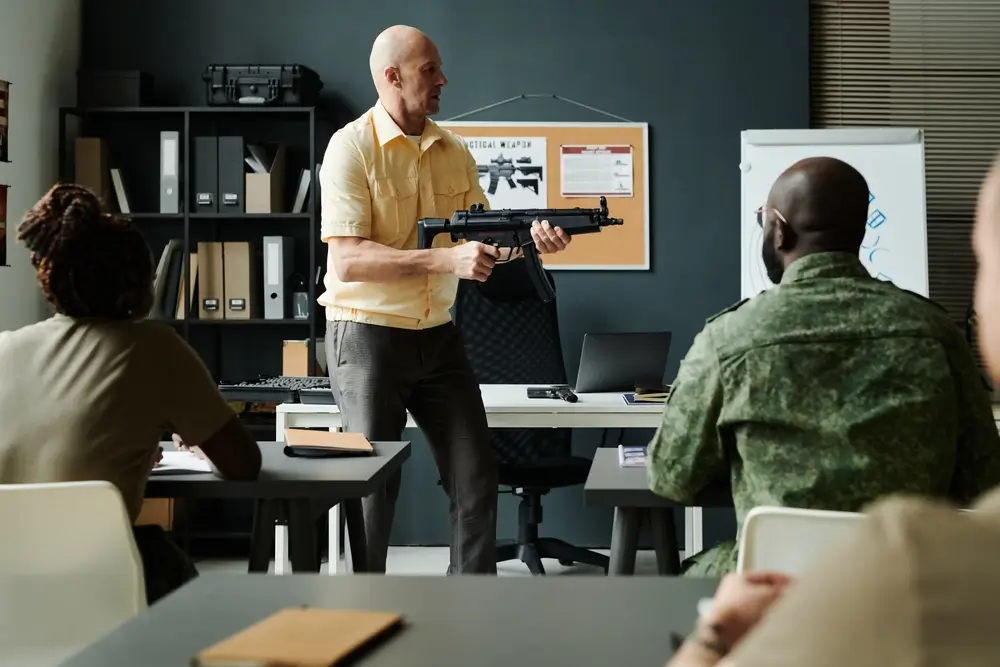 Instructor demonstrating proper rifle handling to military recruits during a weapon training session in a classroom.