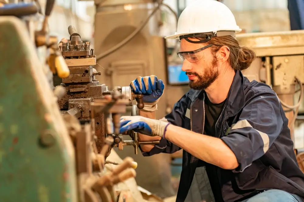 Mechanical engineer operating industrial machinery and inspecting metal parts for a technical trade assessment.