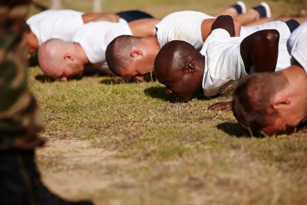 Army recruits performing push-ups on grass during a military fitness assessment.