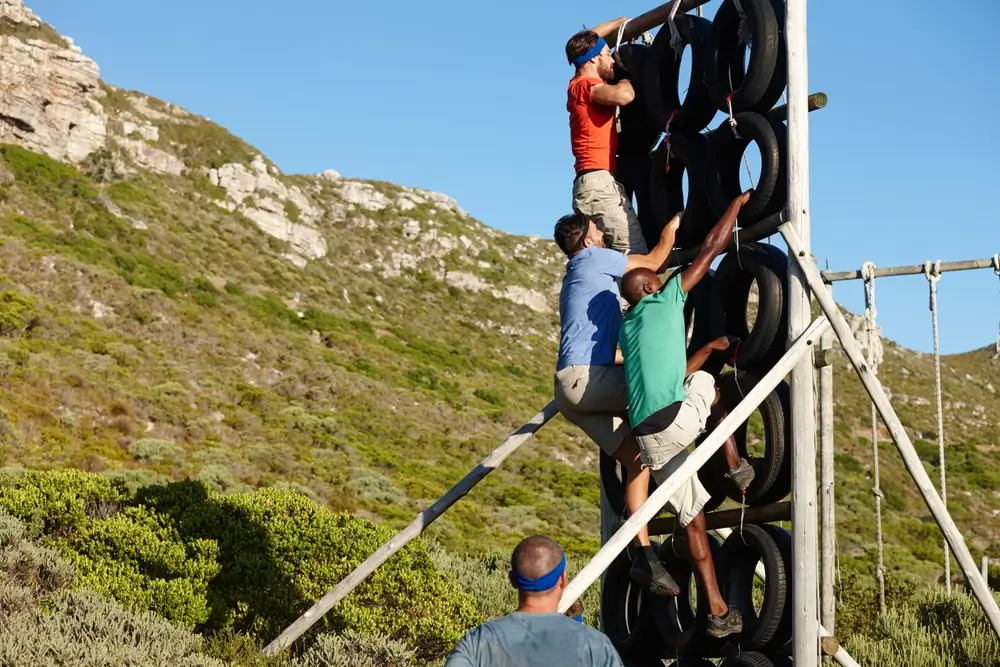 Recruits scaling a tire wall on a military obstacle course during army outdoor fitness training.