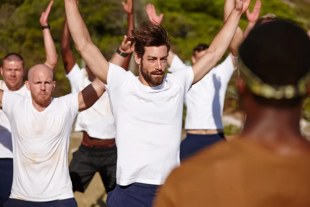 Recruits in white shirts performing jumping jacks during an outdoor military candidates fitness test.