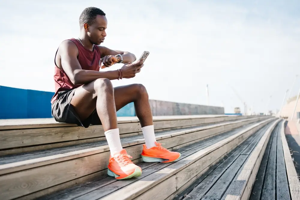 Athlete using a smartphone running app while sitting on stairs to prepare for a beep test fitness training session.