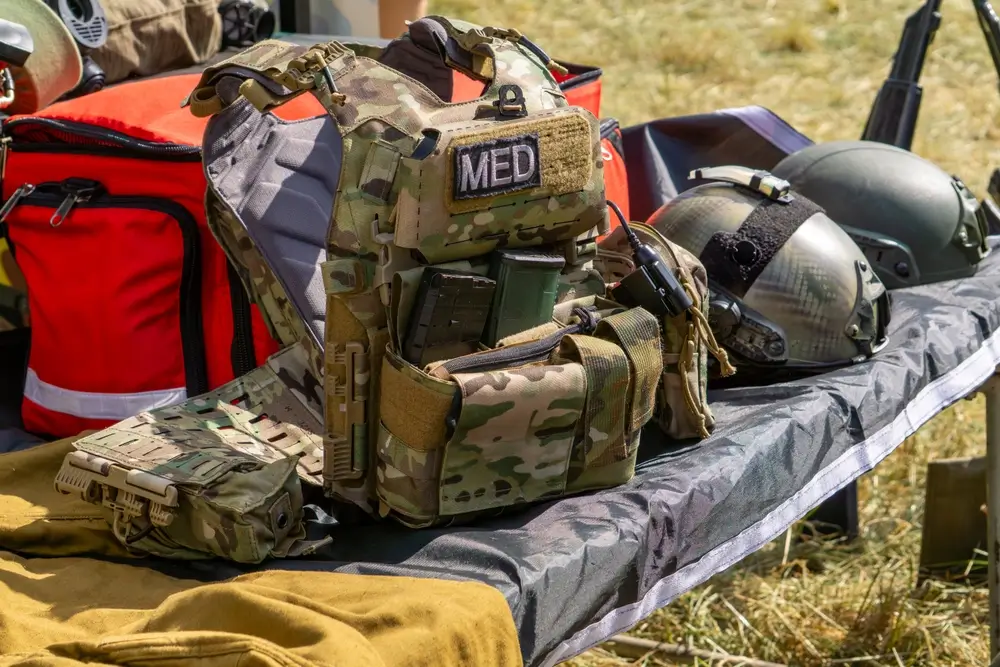 Modern military equipment for infantry combat, including a camouflage medic vest, rifle magazines, and helmets.