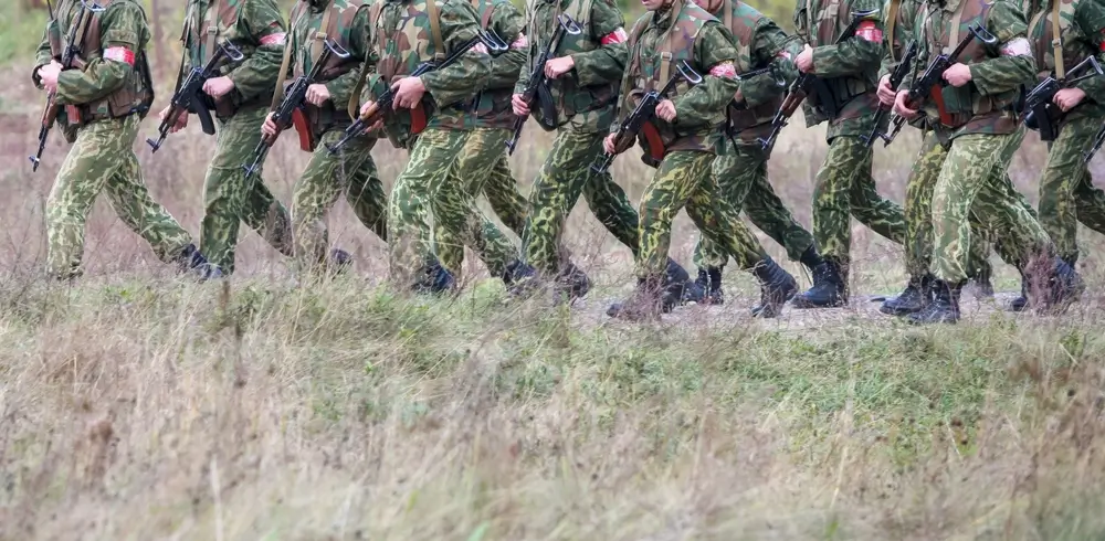 Army recruits in camouflage uniforms marching in formation with rifles during a military drill.