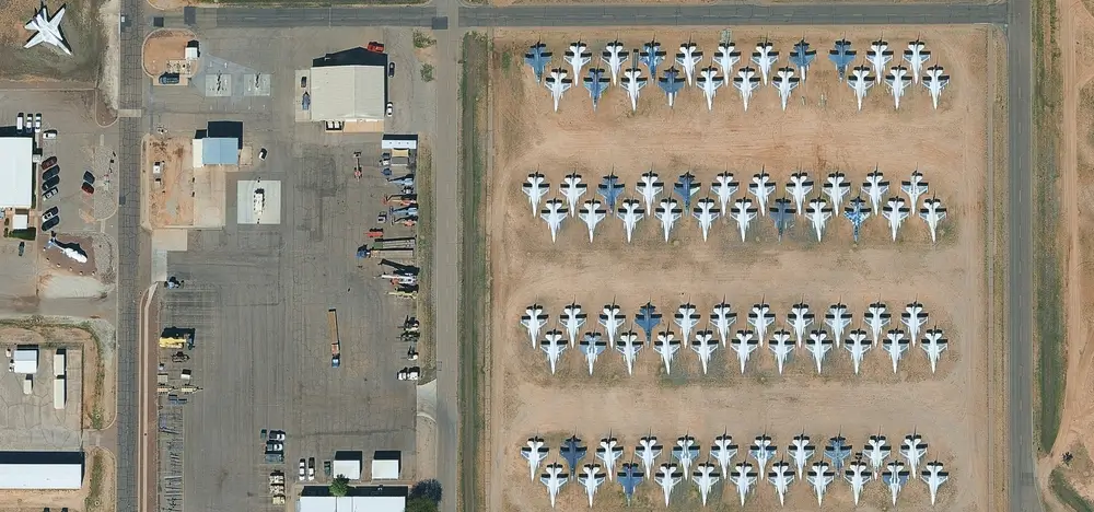 Aerial view of fighter jets parked in rows at a military air force base with hangars and service buildings.