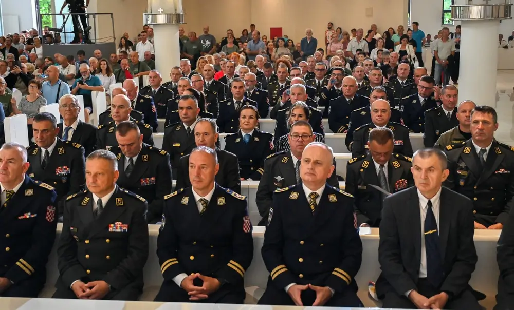 Military personnel in formal dress uniforms seated for a ceremony inside a military mess hall.
