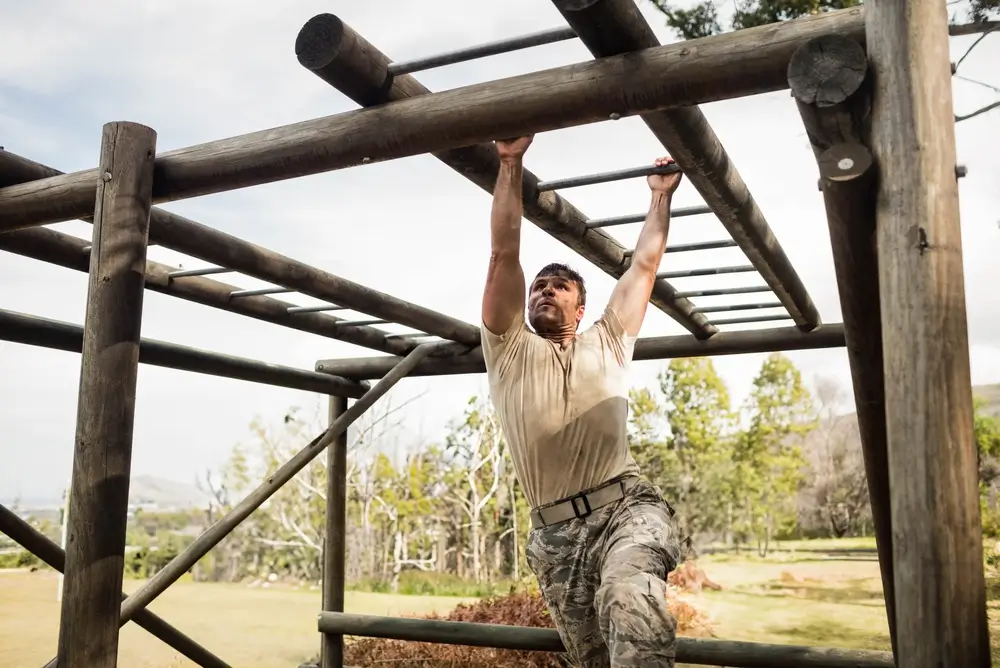 Army recruit navigating wooden monkey bars during physical training on an outdoor obstacle course.