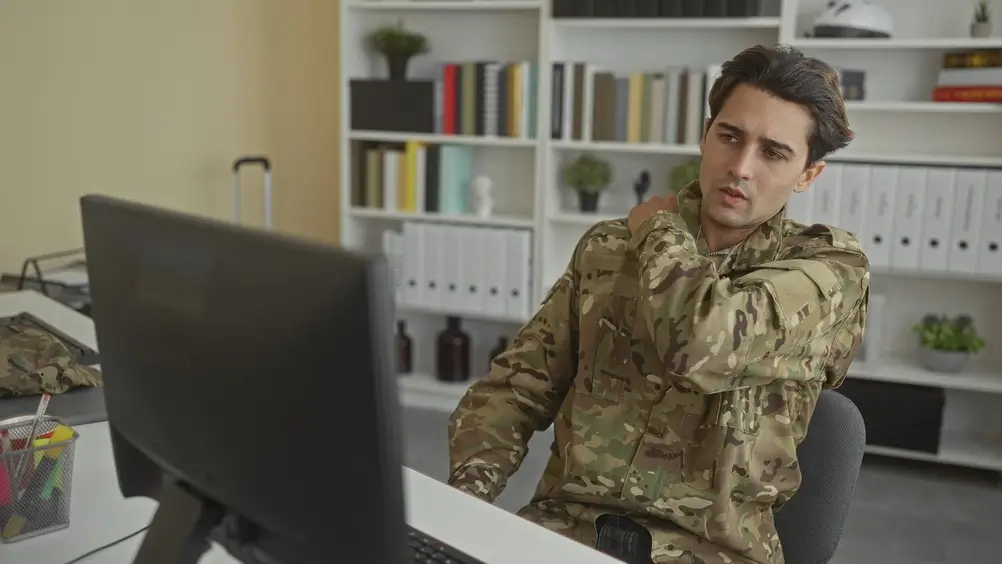 Soldier in uniform reviewing financial planning and military remuneration options on a computer screen at a desk.