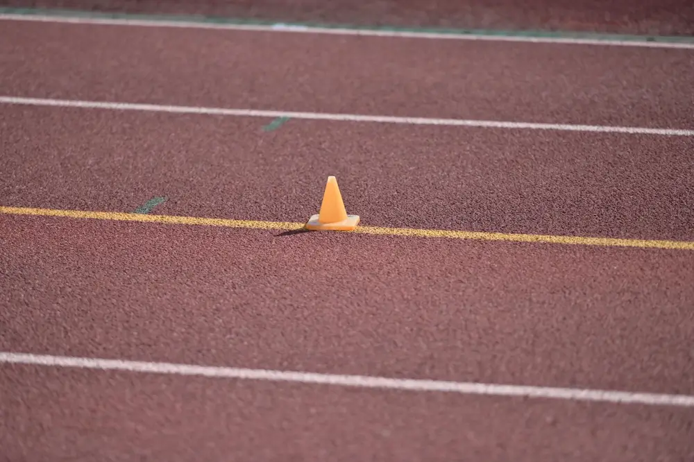 Small orange sports cone on a running track marking the distance for a 20m shuttle run test.