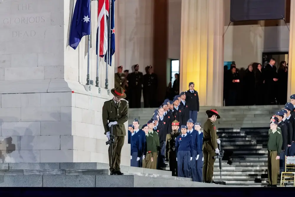 New Zealand Army soldiers in ceremonial service dress and lemon squeezer hats standing in formation at a war memorial.