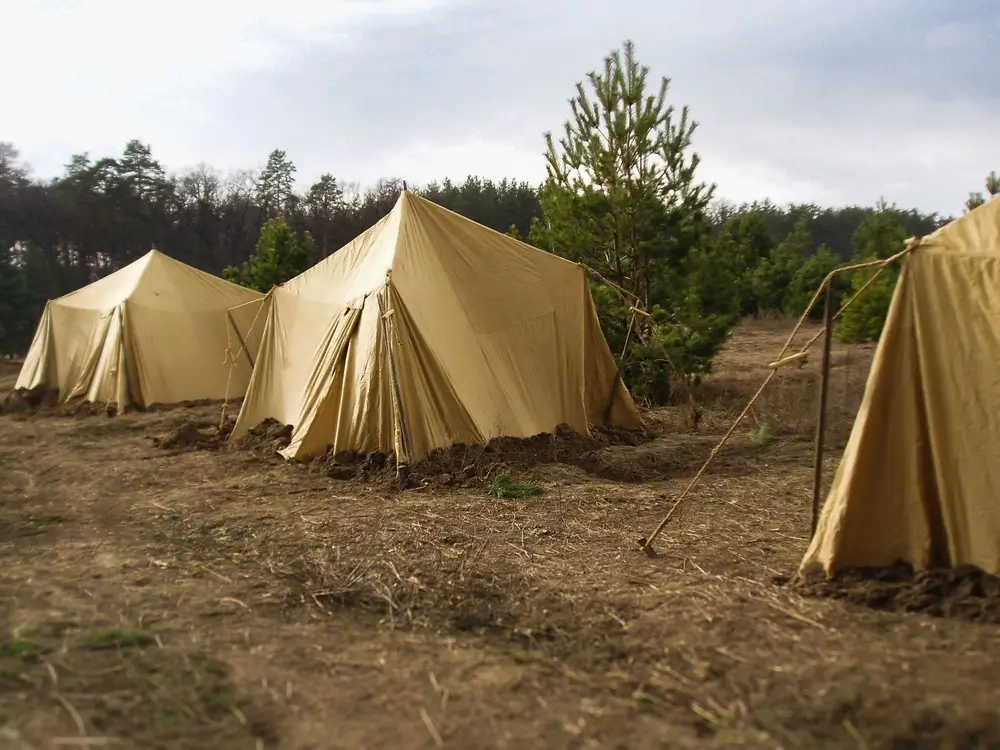 Tan canvas military tents at an army training camp base in a field for collective infantry exercises.