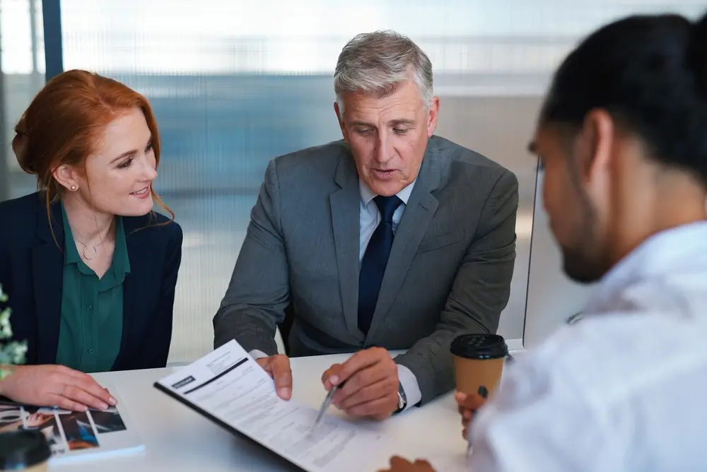 Recruiters discussing career opportunities and salary packages with a young candidate while reviewing a document.