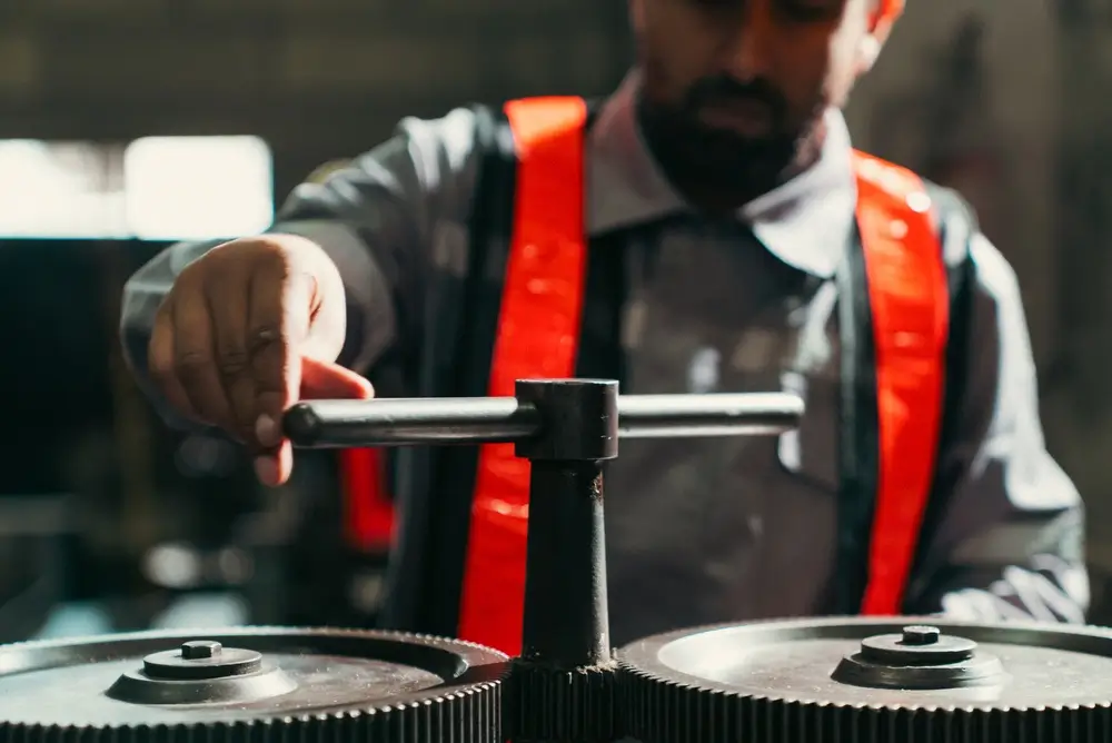 Technician operating a manual lever mechanic tool to rotate industrial gears and apply torque in a factory.
