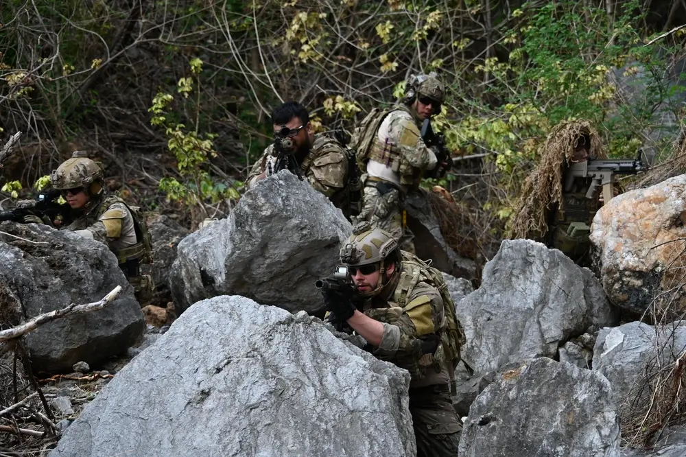 Infantry soldiers in tactical gear maneuver through rocky terrain during a military patrol field training exercise.