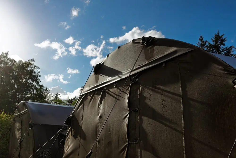Olive green tents set up at a military training camp army base under a bright blue sky.