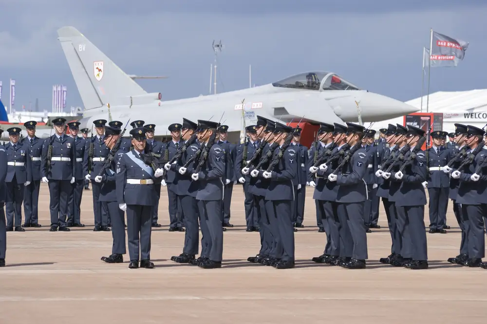 RNZAF recruits in uniform stand in formation with rifles during a military parade in front of a fighter jet.