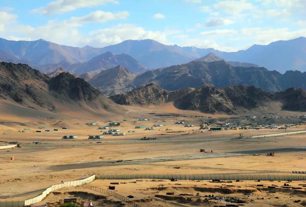 Remote military base field camp with tents and a landing strip in a rugged desert landscape for relief operations.