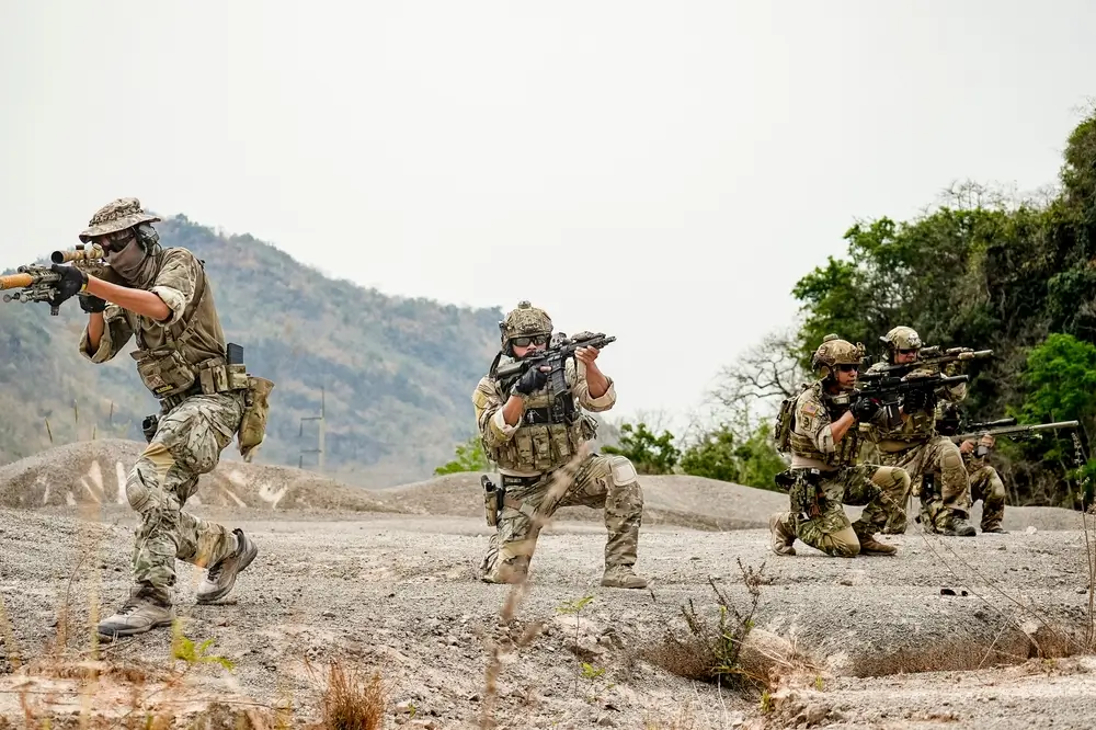 Army infantry soldiers in camouflage gear conduct tactical maneuvers during a field military training exercise.