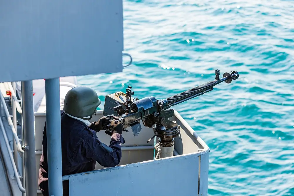 Navy sailor manning a mounted gun on a warship deck while patrolling for maritime security and surveillance.
